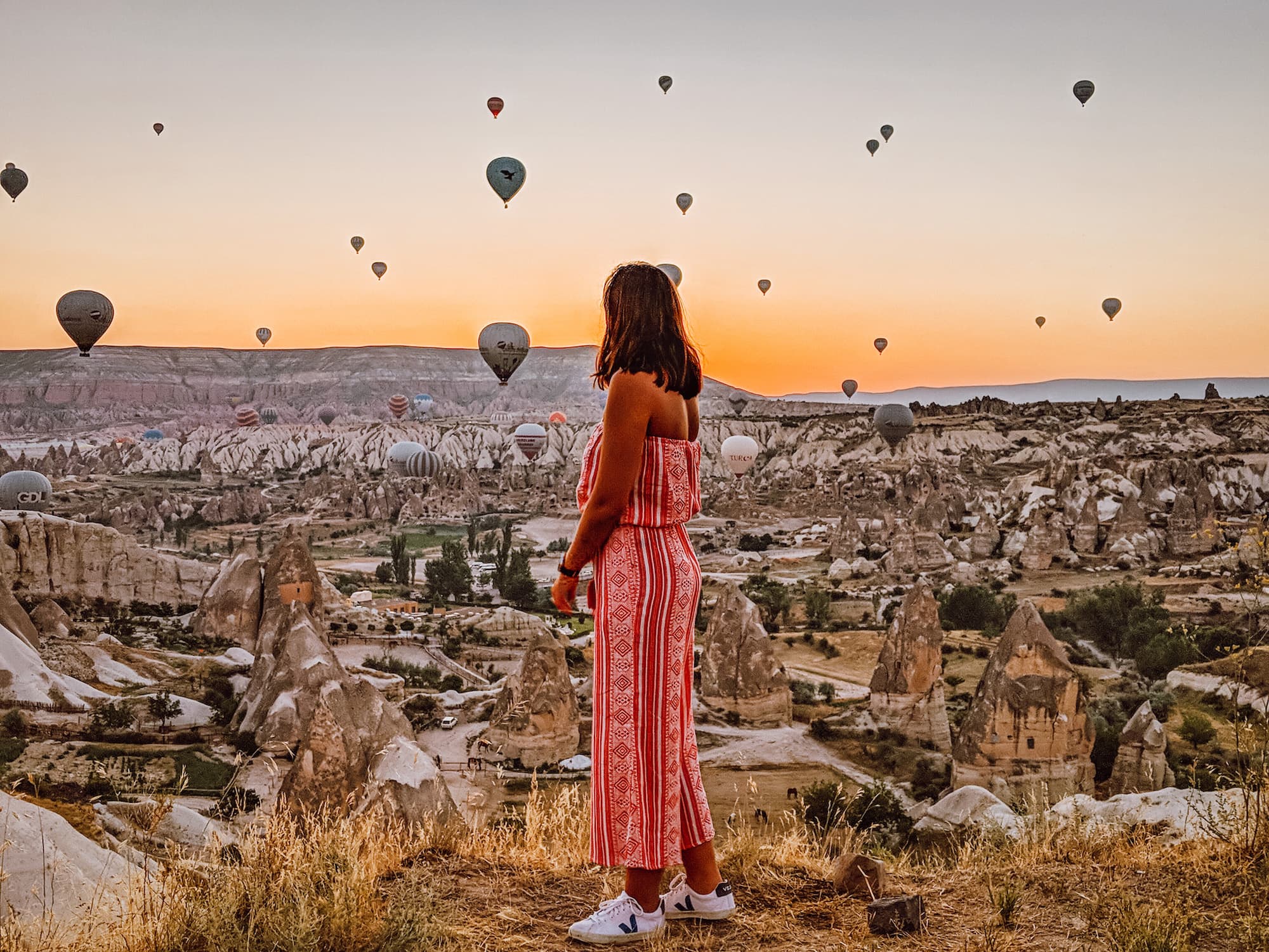 Girl looks out over sky full of hot air balloons in Cappadocia