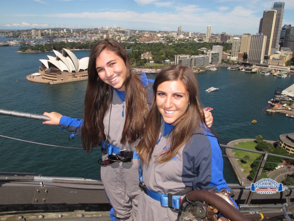 Two girls standing on top of Sydney bridge with opera house & skyline in back