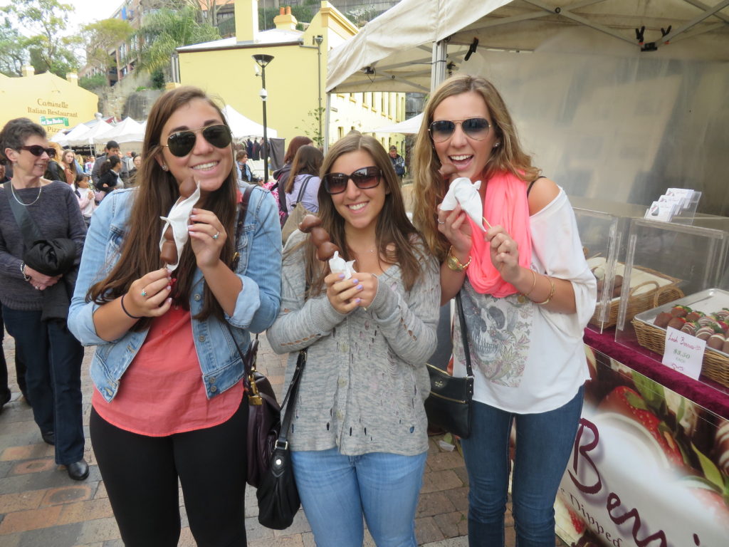 Three girls eating chocolate covered strawberrys in market