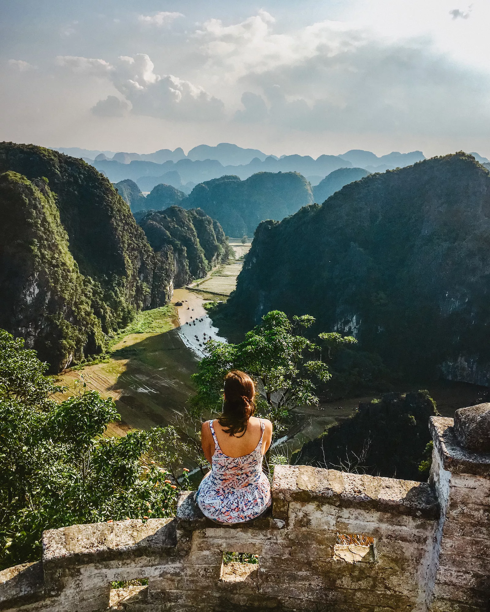 girl sitting on ledge looking over limestone hills and river in Tam Coc at Hua Mang Peak