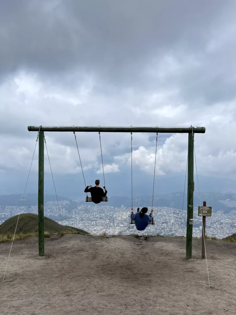 two people swinging over views of Quito