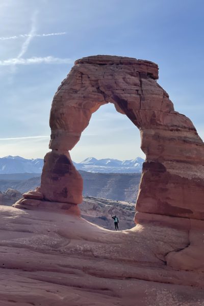 Girl standing under Delicate Arch looking out at La Sal Mountains