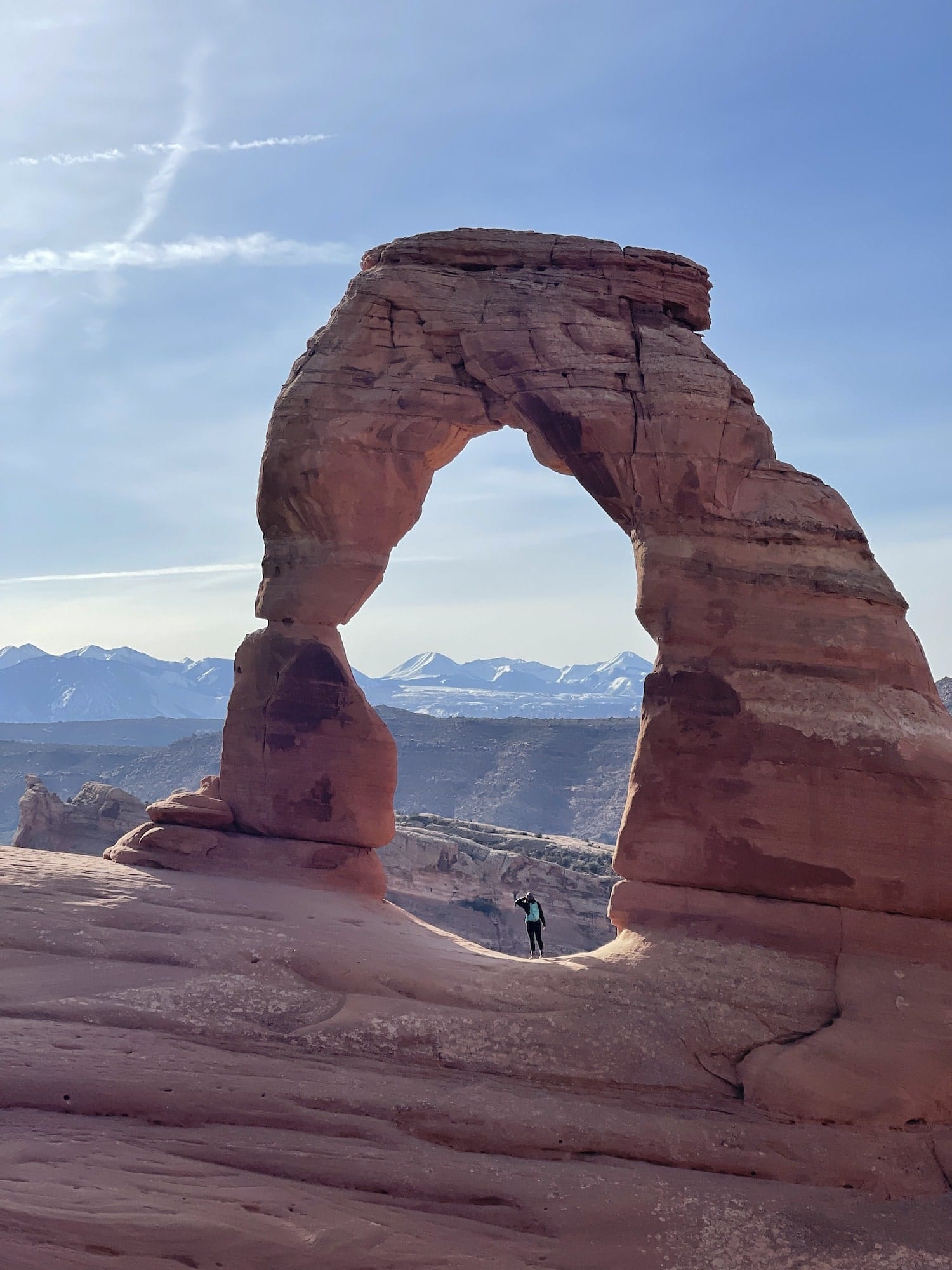 Girl standing under Delicate Arch looking out at La Sal Mountains