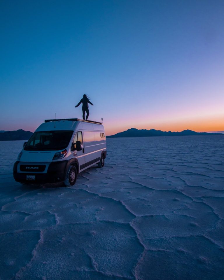 girl watching sunrise at bonneville salt flats from roof of campervan