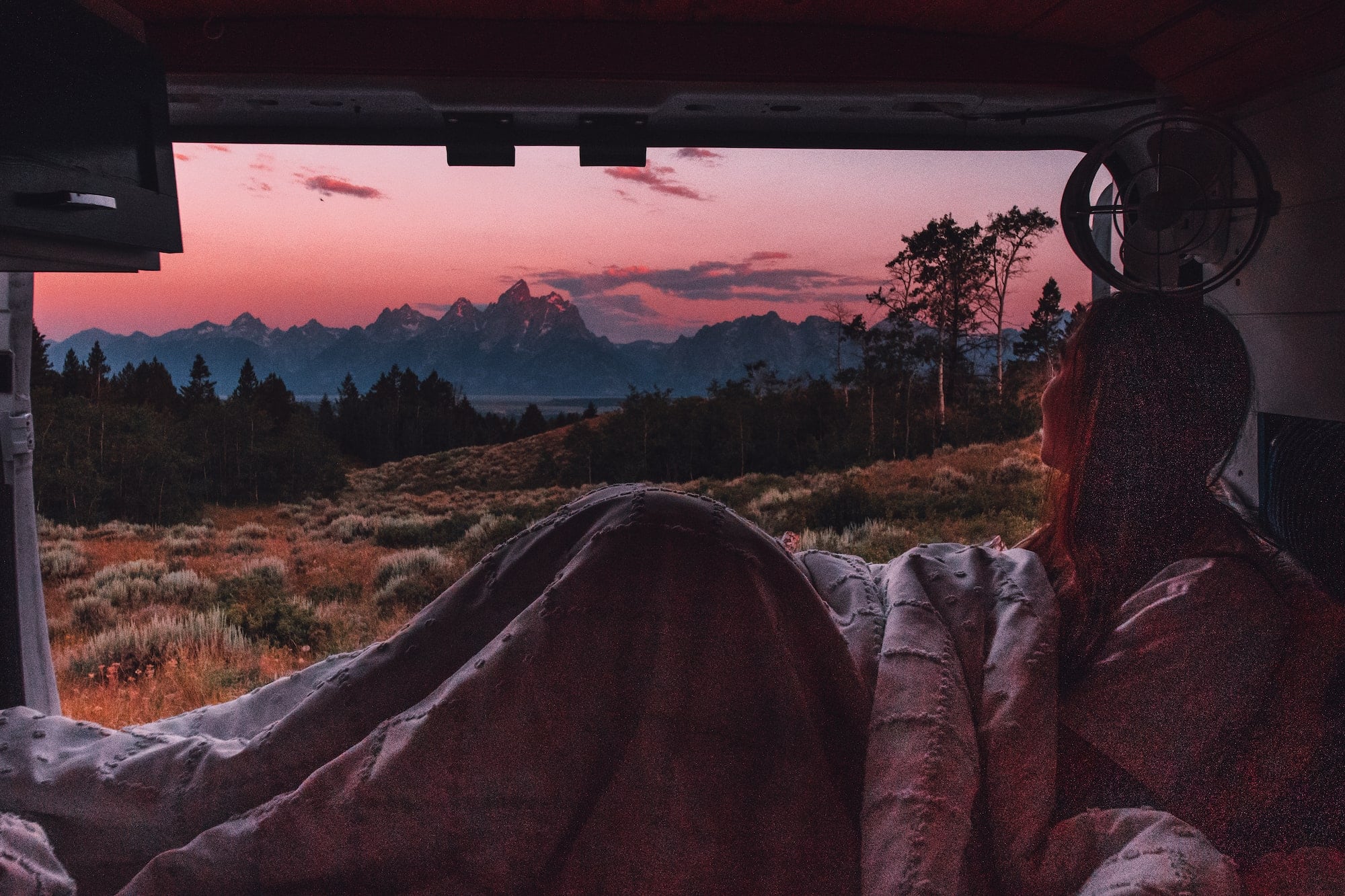 girl watching sunrise over tetons from bed