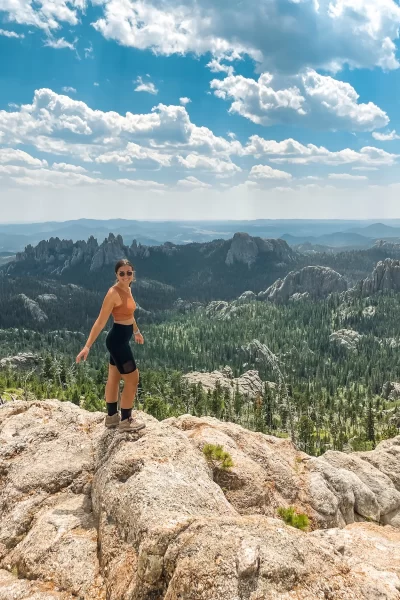 girl on top of black elk peak in south dakota with black hills rising up behind