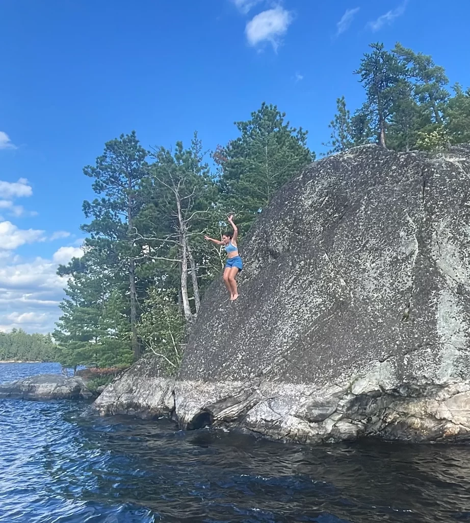 girl mid air after cliff jumping off large cliff that extends into the water