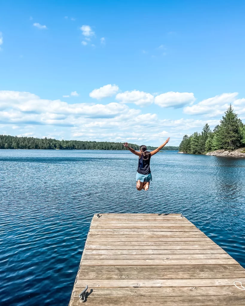 girl jumping on a dock with Lake Superior in front of her, waters of Voyageurs National Park