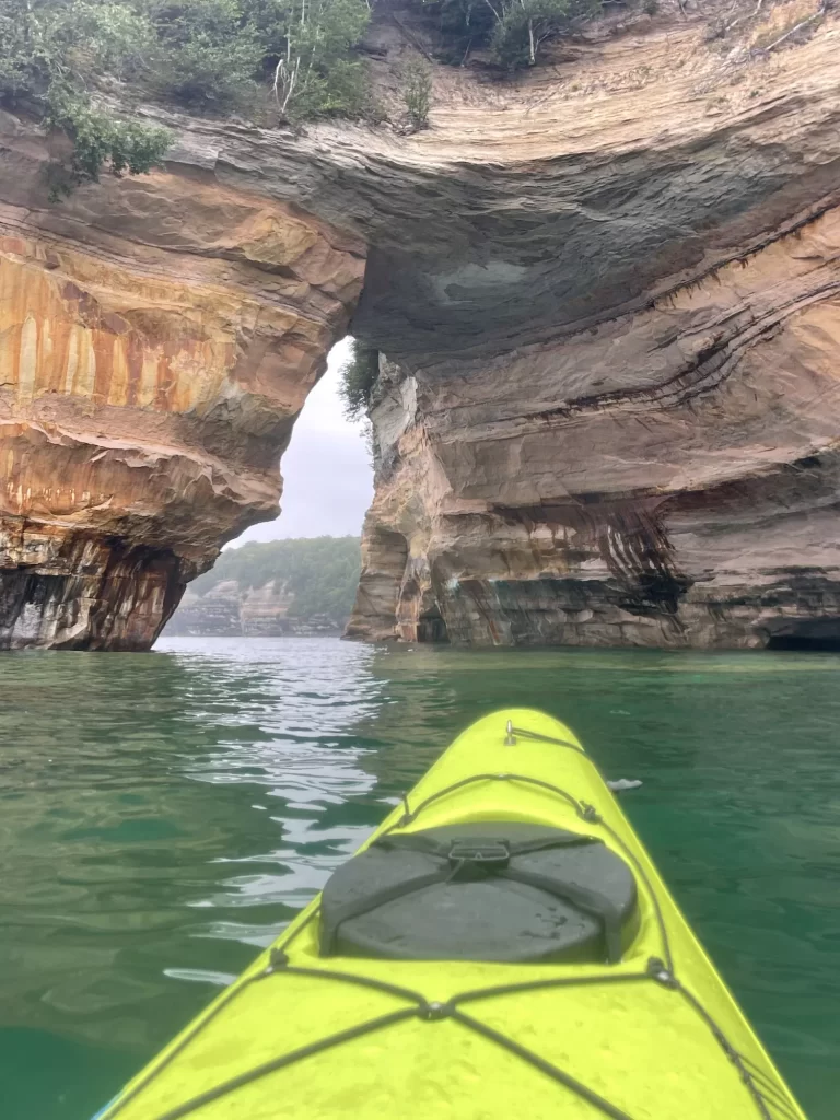 kayak in waters near pictured rocks with opening through the rocks to rocks in the distance