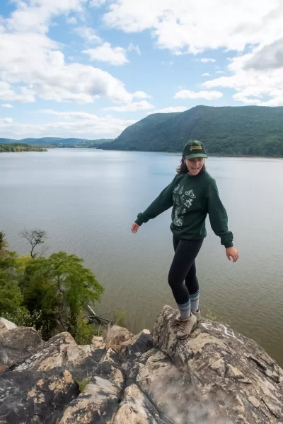 girl standing on summit of breakneck ridge above hudson river. she is standing with arms out and tongue out