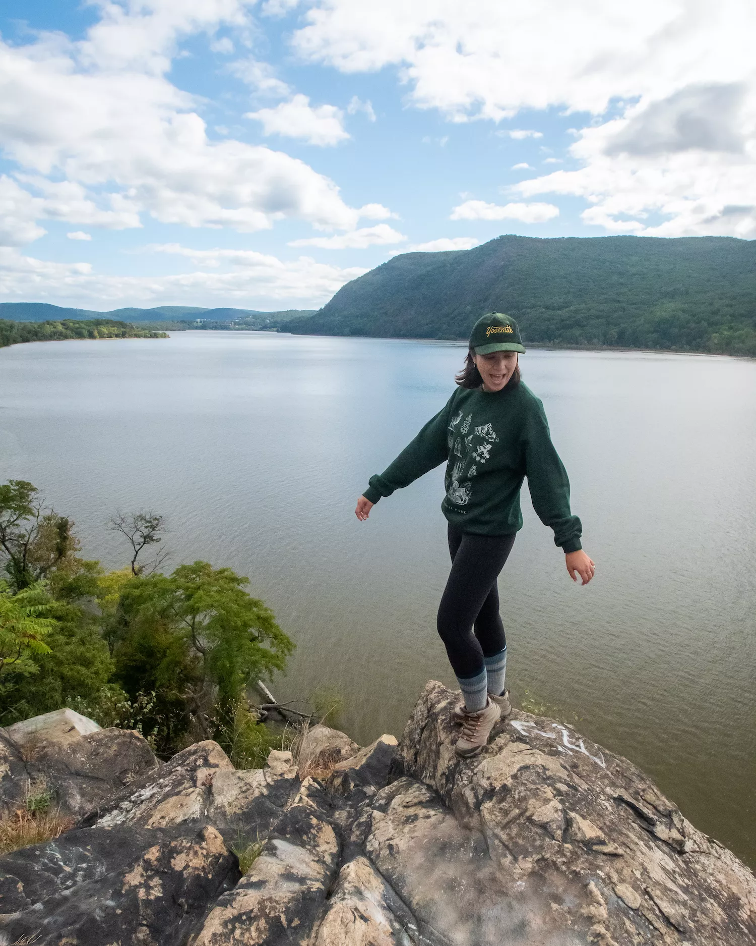 girl standing on summit of breakneck ridge above hudson river. she is standing with arms out and tongue out