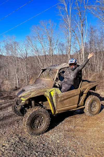 Girl sitting on edge of ATV with hands up on the ridge line of Hatfield McCoy Trail