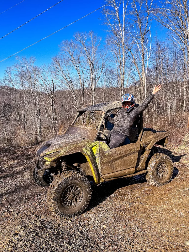 Girl sitting on edge of ATV with hands up on the ridge line of Hatfield McCoy Trail