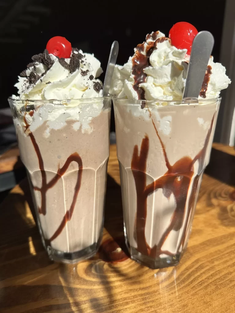 Two chocolate milkshakes with whipped cream and cherries