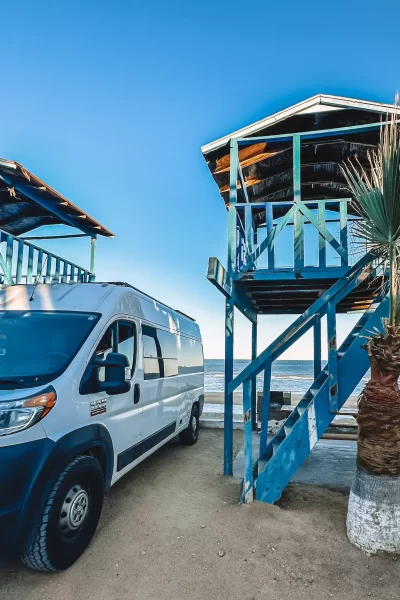 van next to a palapa in baja mexico with ocean behind