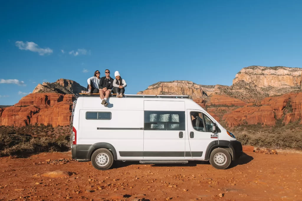 people sitting on a van in front of sedona red rocks