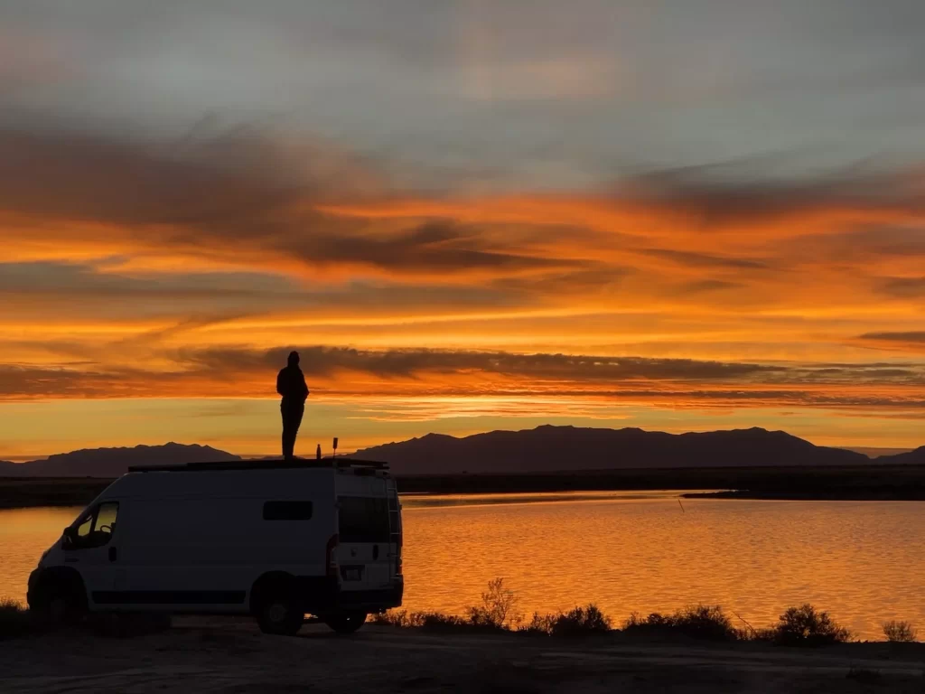 girl standing on van with sunset behind her