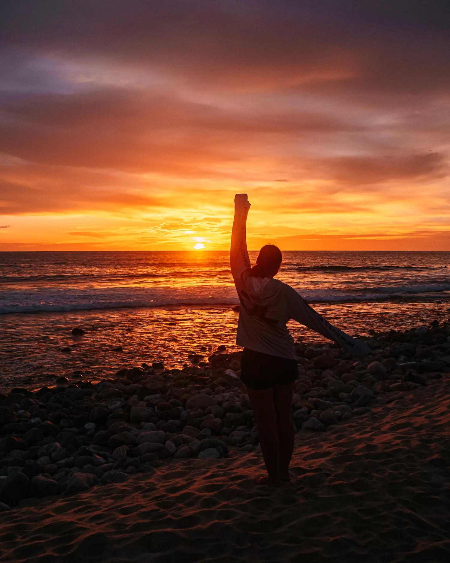 girl with arms up in front of the sunset at san pedrito beach in todos santos