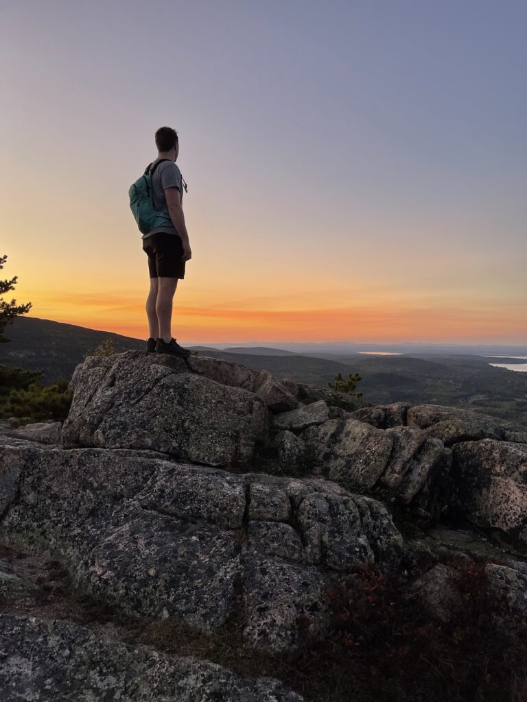 boy standing on a boulder with sunset behind them