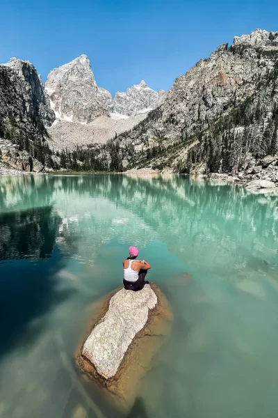 girl sitting on a rock in the middle of an alpine lake in grand teton national park