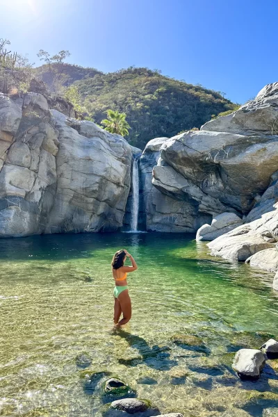 girl standing in swimming hole with waterfall behind her at cañón de la zorra