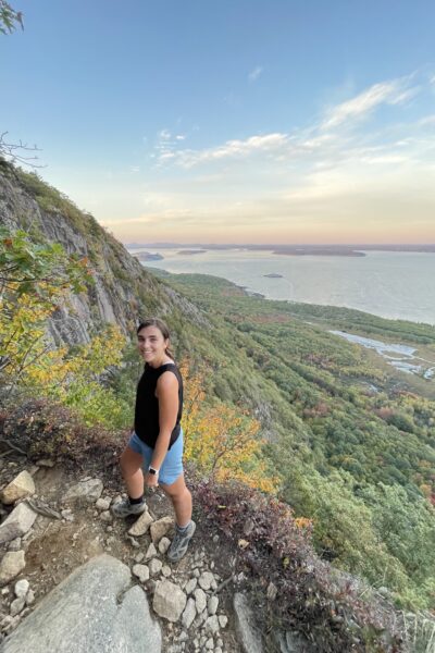 girl standing on the cliff edge of precipice loop trail in acadia with frenchmans bay beyond