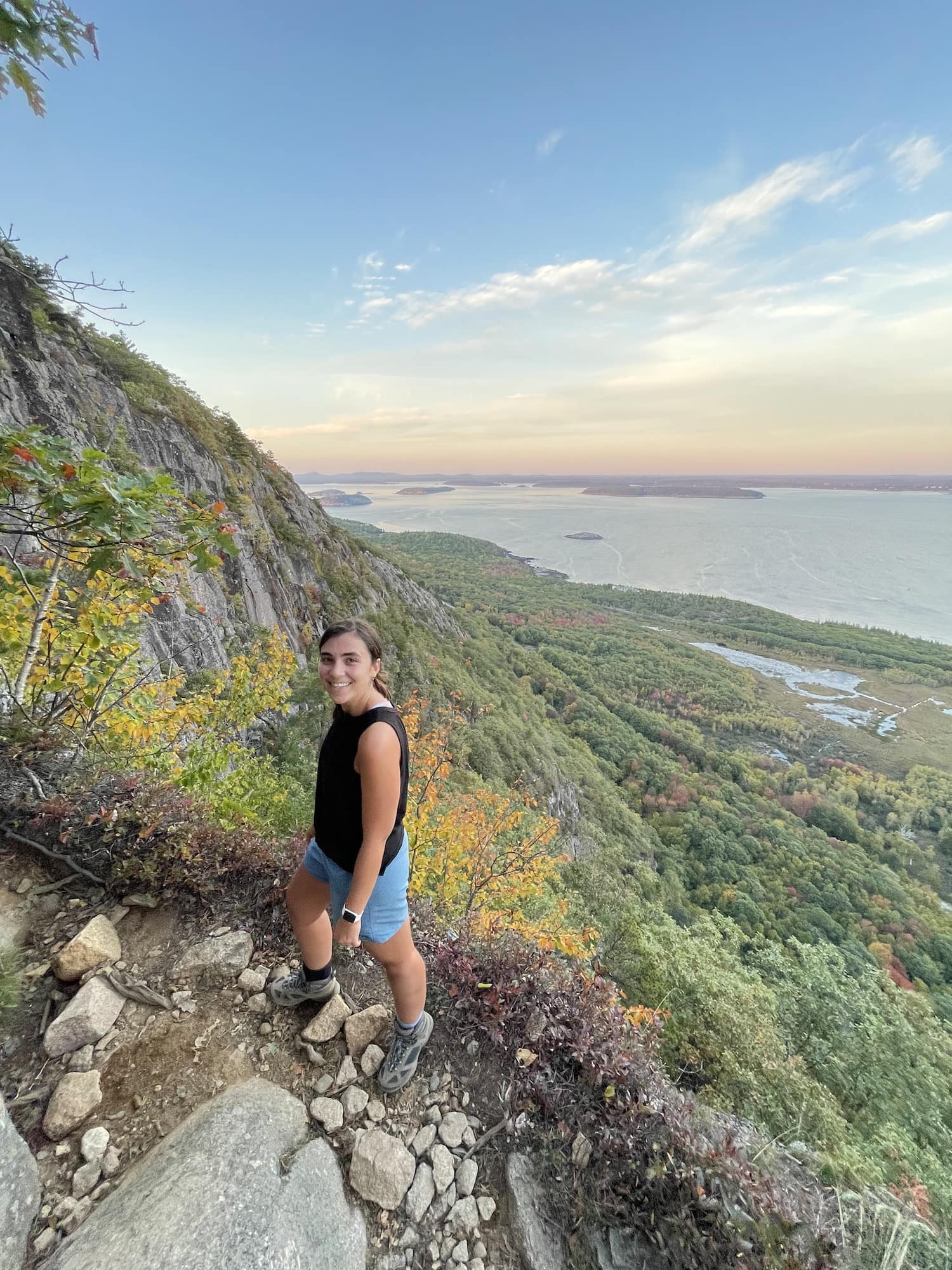 girl standing on the cliff edge of precipice loop trail in acadia with frenchmans bay beyond