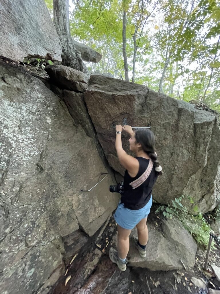 girl holding onto an iron rung on a boulder in precipice