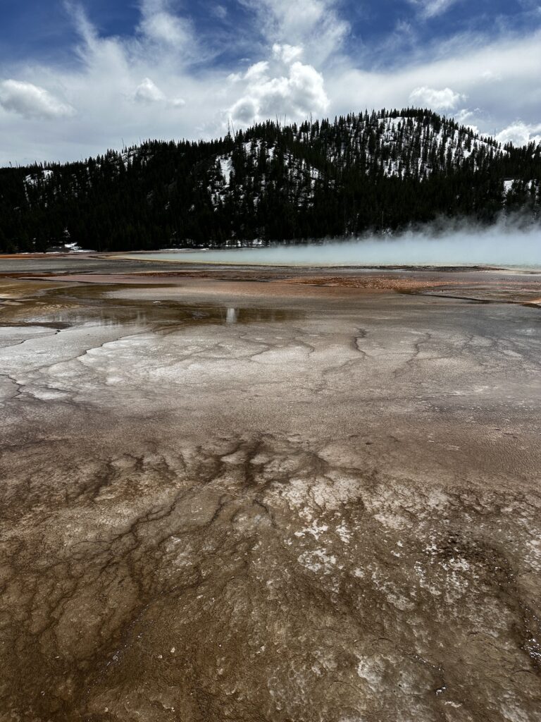 ground turning from brown to orange until you get to the blue of the grand prismatic spring, steam comes up above it