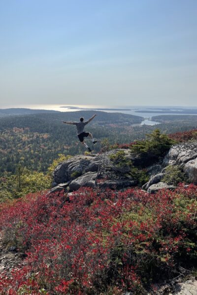 boy jumping and kicking his foot above Acadia on Sargent Mountain