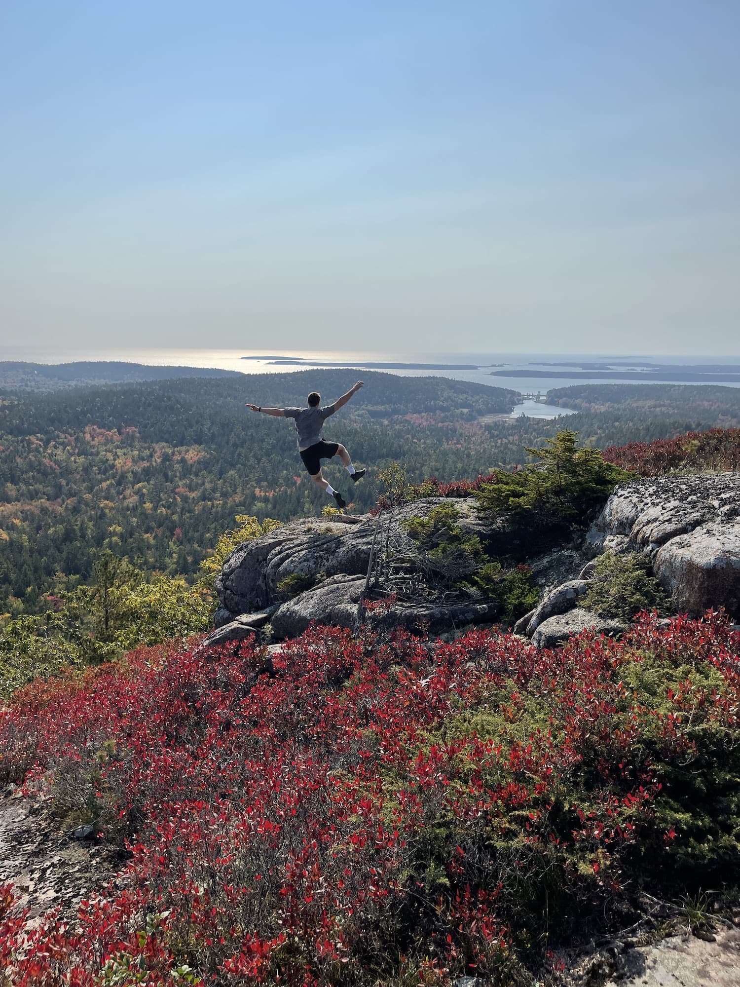 boy jumping and kicking his foot above Acadia on Sargent Mountain