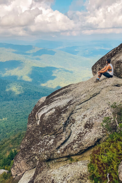 girl sitting on the top of old rag mountain summit with green trees behind