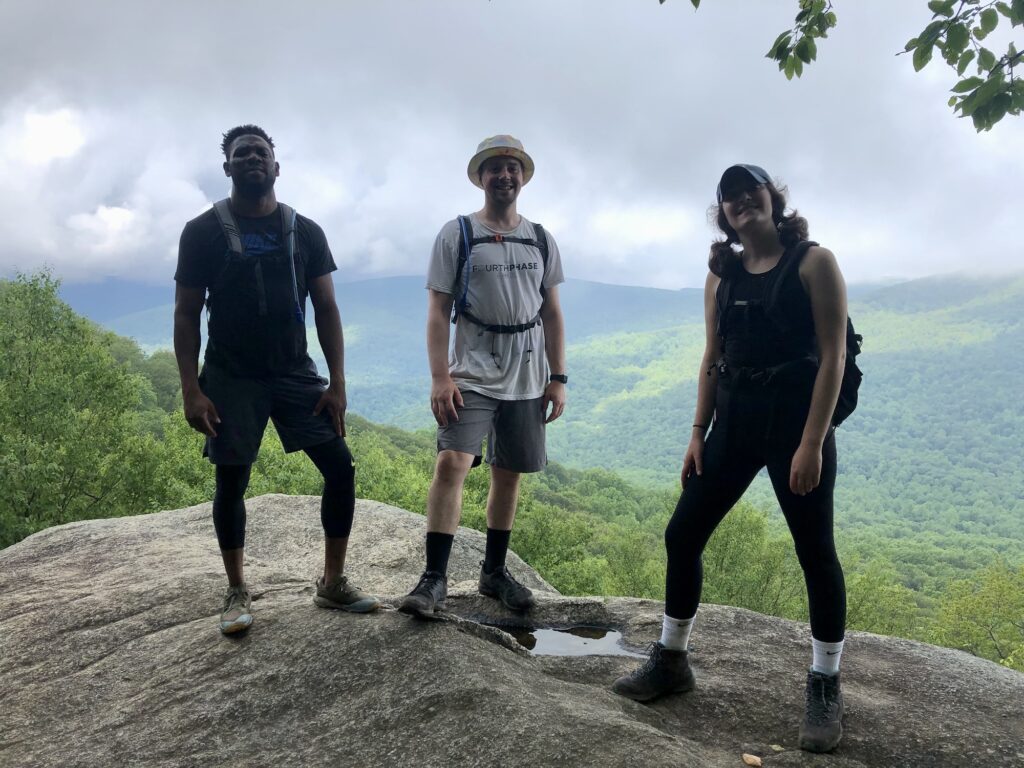 three people standing on a boulder with backpacks on