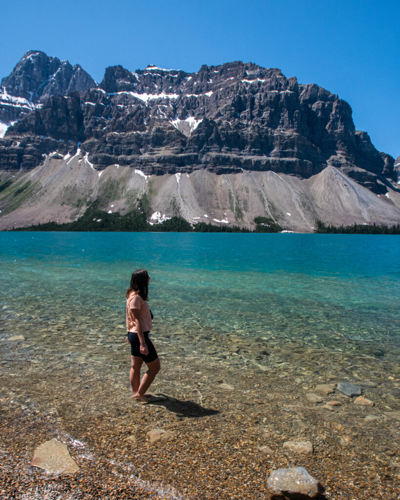 Girl standing in blue water of Bow Lake with mountain behind her