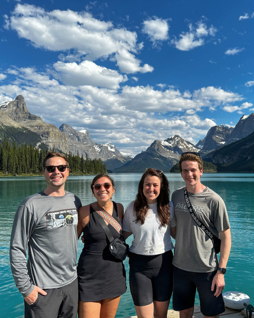 four people standing in front of bright blue lake