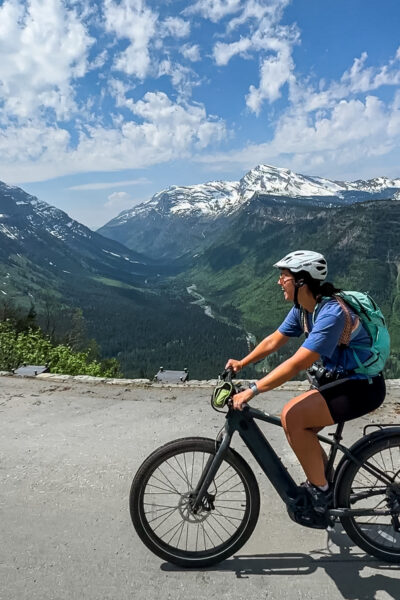 girl biking the going to the sun road in Glacier National Park with mountain views behind her