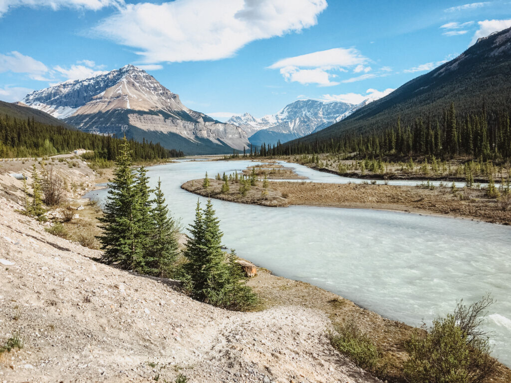 view of icy blue water cutting through Rocky Mountains off Icefields Parkway