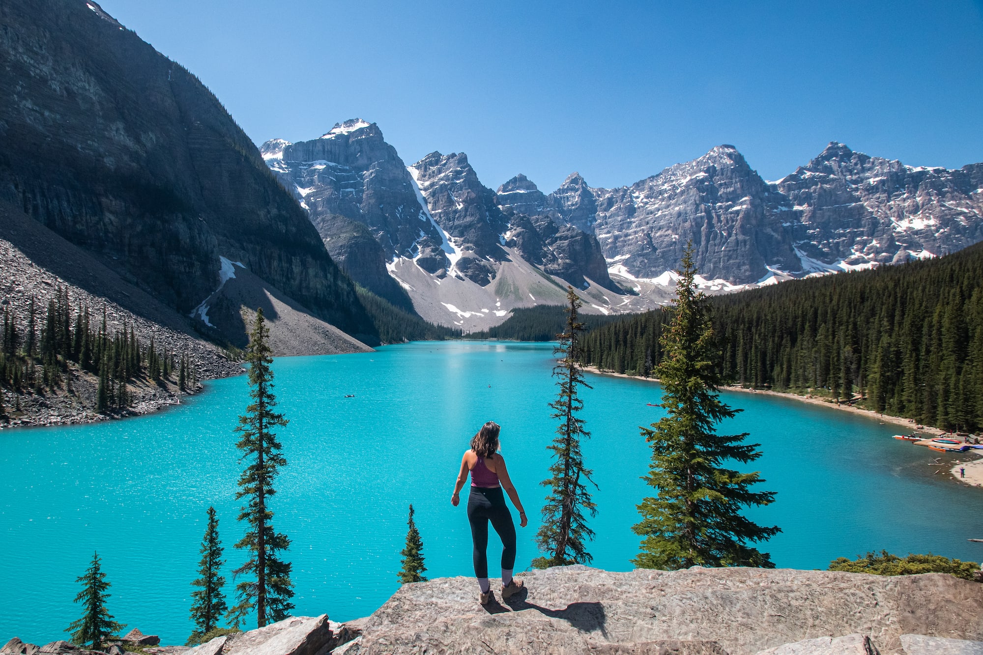 Girl standing at moraine lake with stunning blue color and mountain peaks behind her