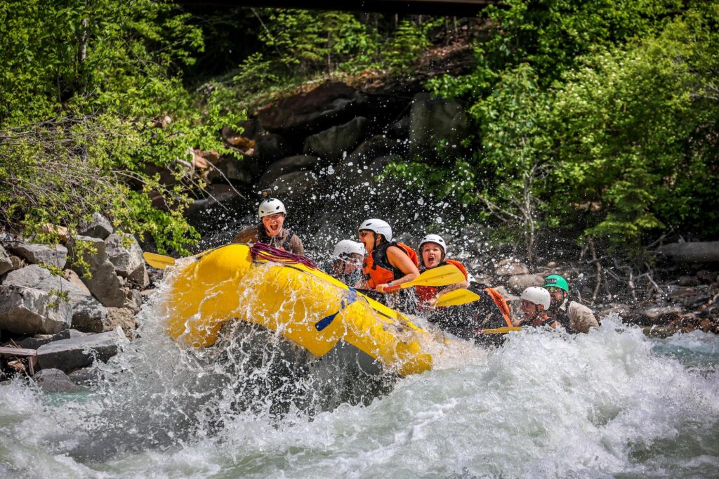 raft of people going through whitewater with everyone smiling as a wave is about to hit them