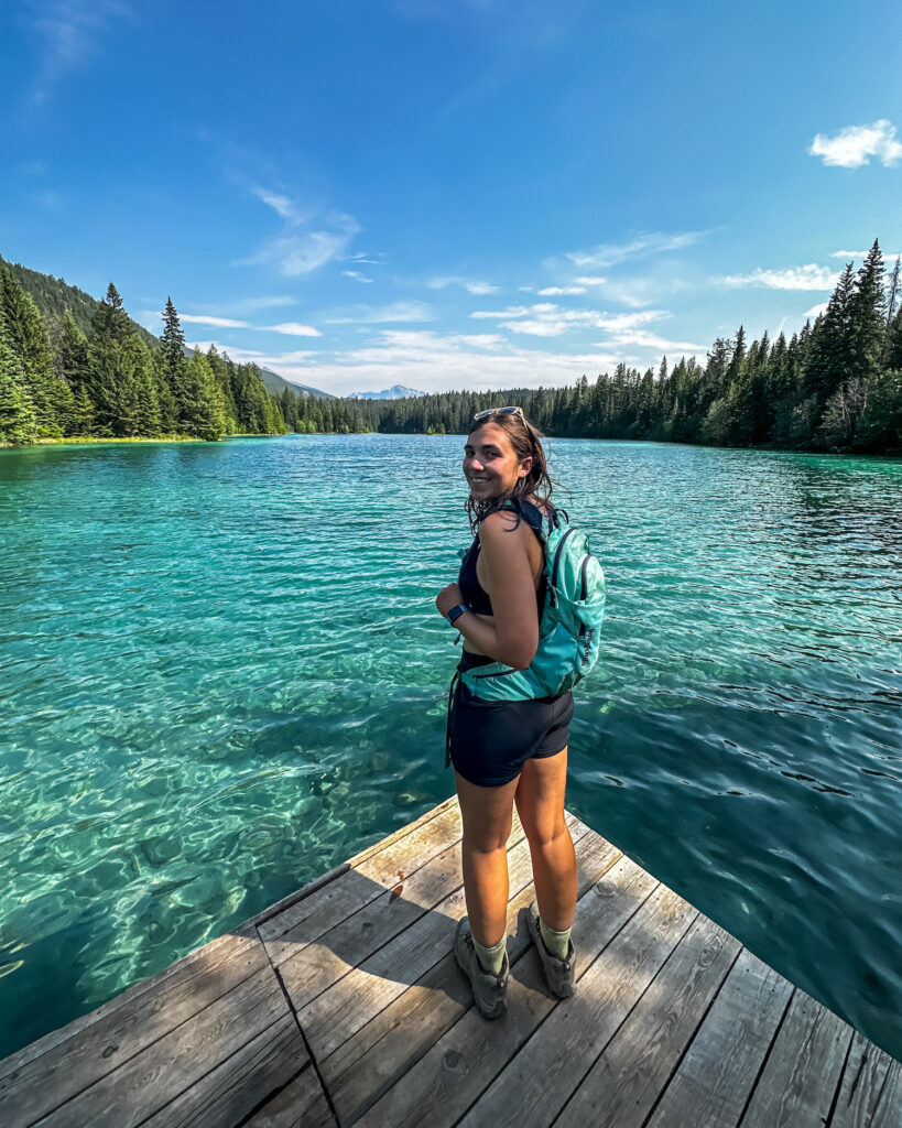 Girl smiling and looking back while standing on a dock of a bright blue lake