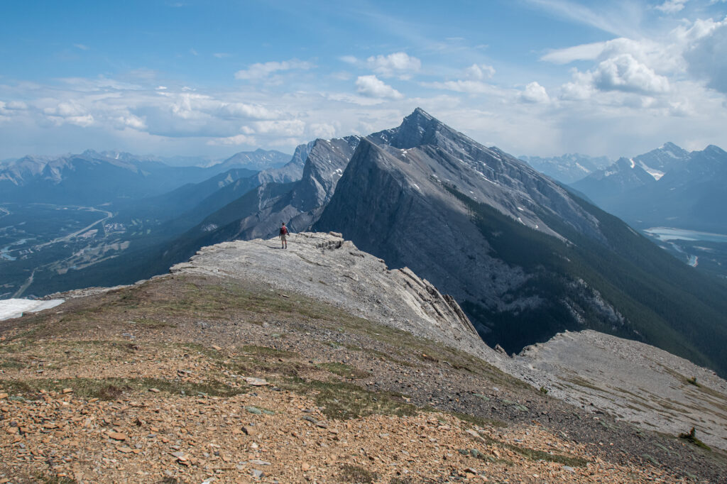 boy walking to the edge of a mountain with tall mountain peaks rising above him