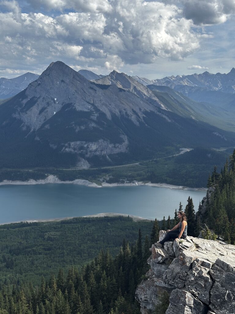 girl sitting on a mountain summit with blue lake below and other mountain across