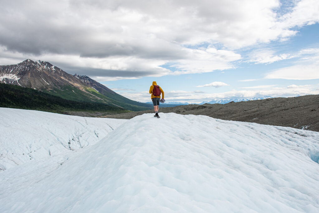 boy walking on a glacier with mountains behind him