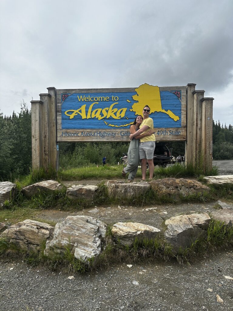 two people hugging at the welcome to alaska sign