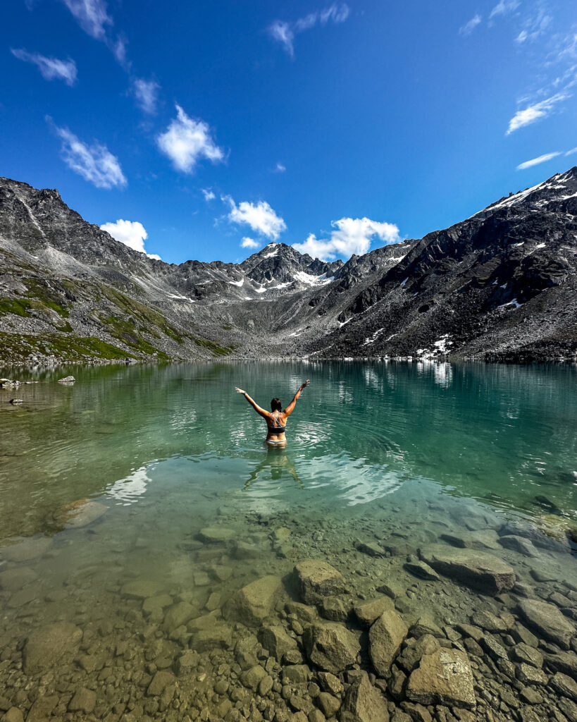 Girl in water of Upper Reed Lakes with mountain above her and her arms up