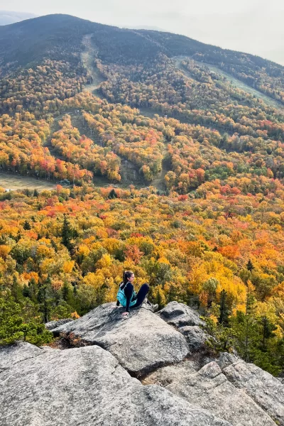 girl sitting on a mountain in franconia notch park with fall colored trees all around