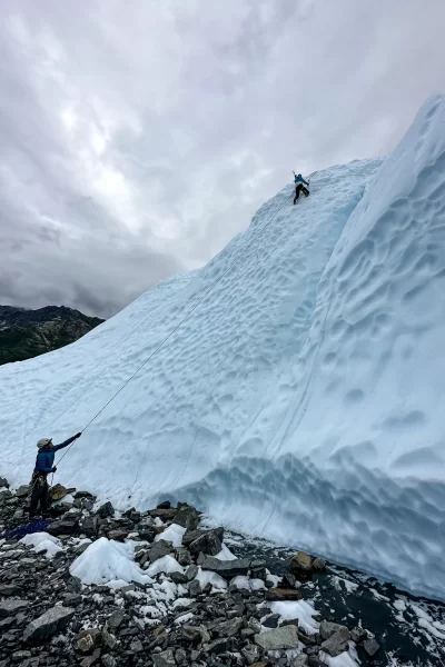 girl climbing up a glacier with a guide belaying her