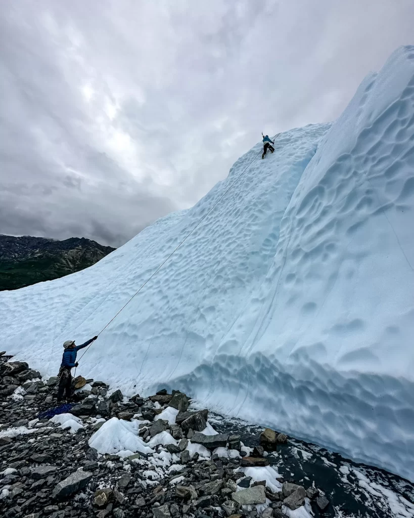 girl climbing up a glacier with a guide belaying her