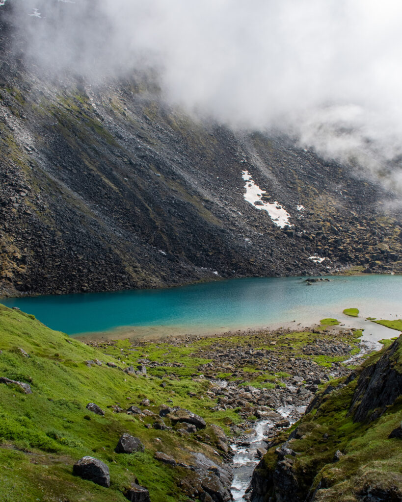 blue lake with green ground and fogged in mountains