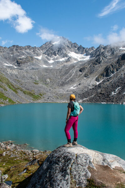 girl standing on a rock above reed lakes with the bright blue water behind her